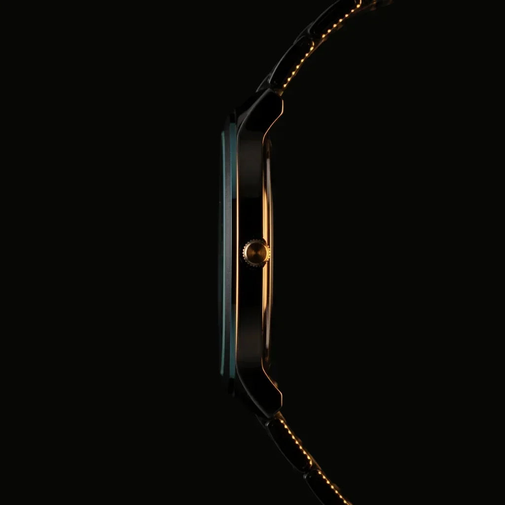 Slim black analog watch with gold accents and stitched strap, side view on dark background