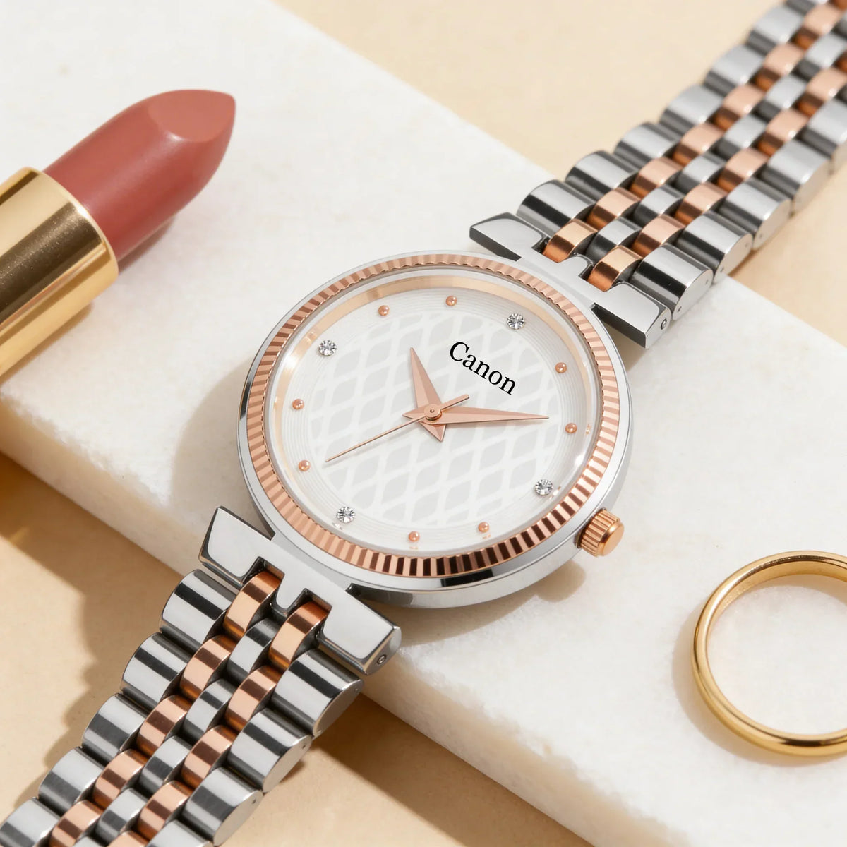 Elegant two-tone women’s analog wristwatch with white patterned dial, rose gold accents, shown beside lipstick and gold ring.