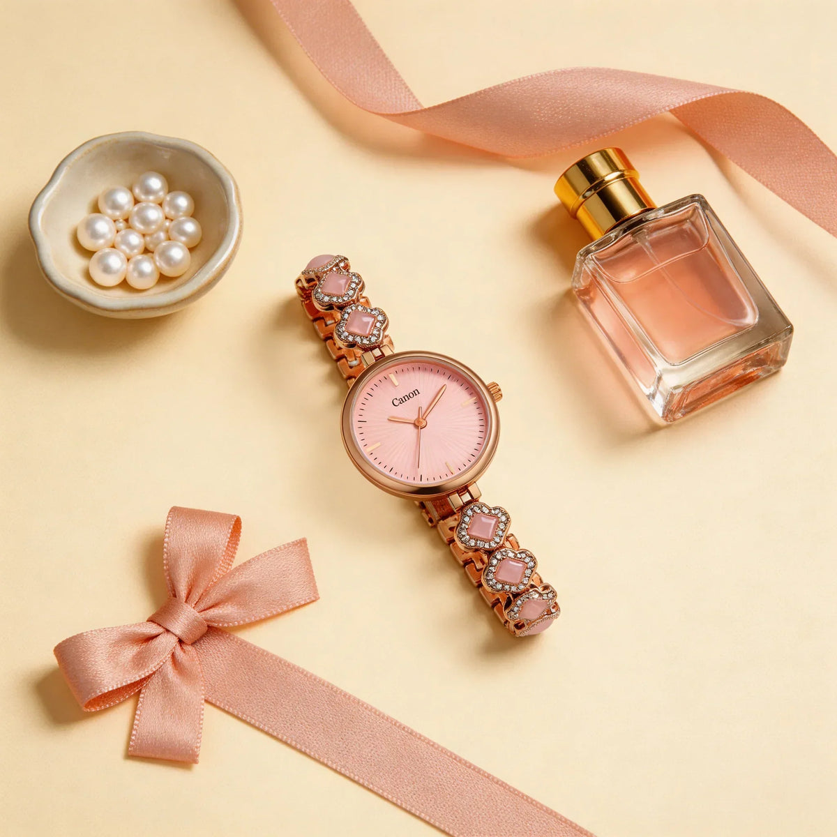 Elegant women's rose gold analog watch with pink dial and bracelet, pearls, perfume, and ribbon arrangement.