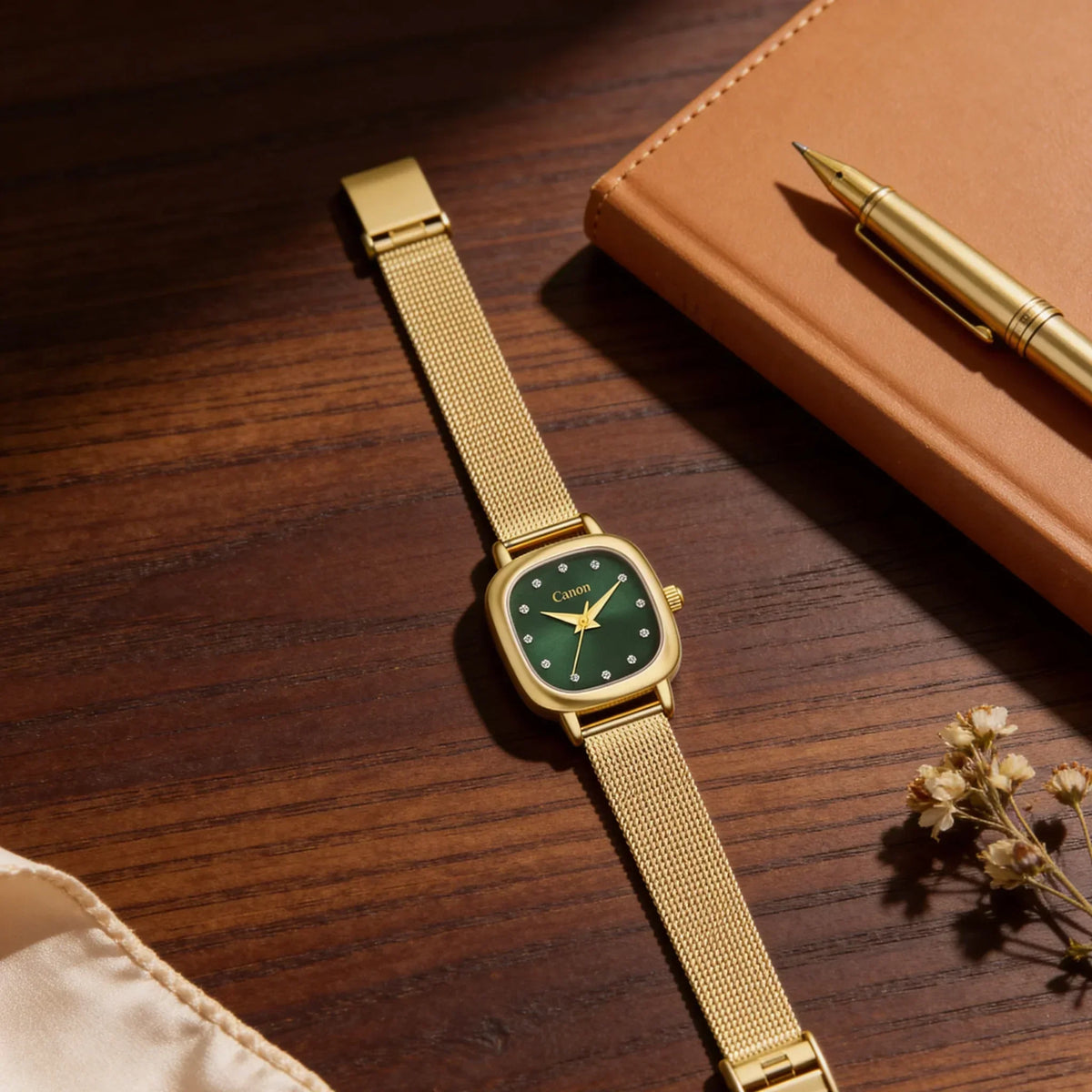 Elegant gold mesh strap watch with green dial and diamond markers, styled with notebook and pen on wood desk
