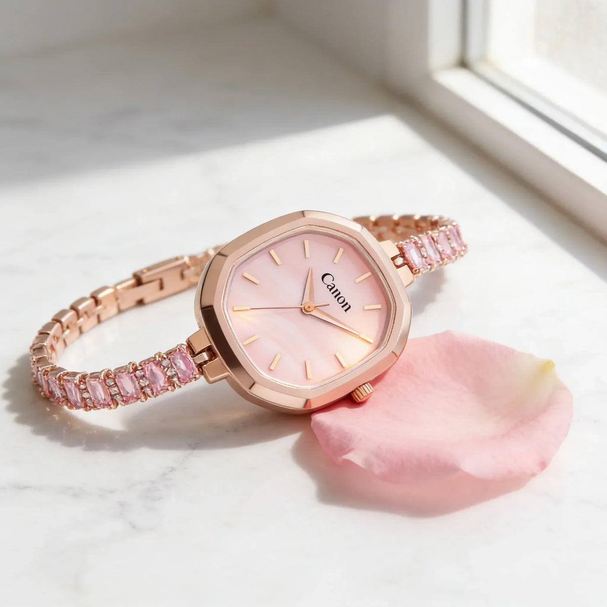 Rose gold analog women's watch with pink face and jeweled bracelet on marble by a window