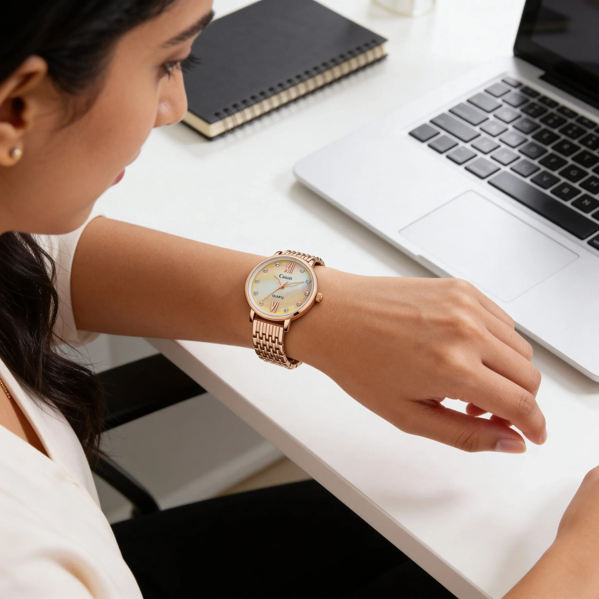 Woman at desk wearing elegant gold analog watch with round white face and Roman numerals