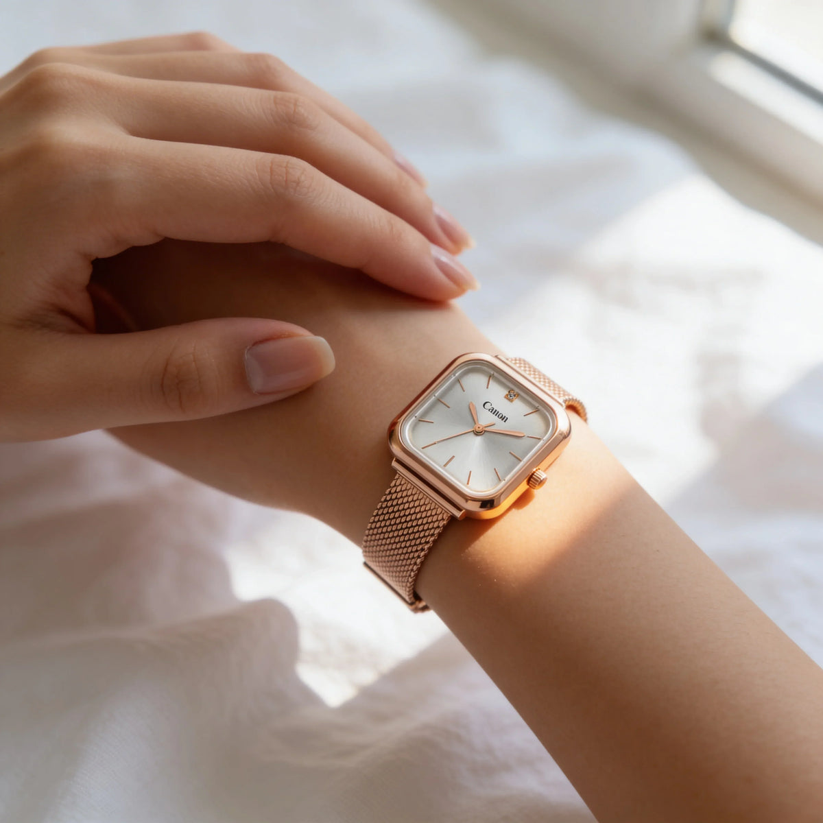 Elegant rose gold square analog watch with mesh strap on a woman's wrist in natural light