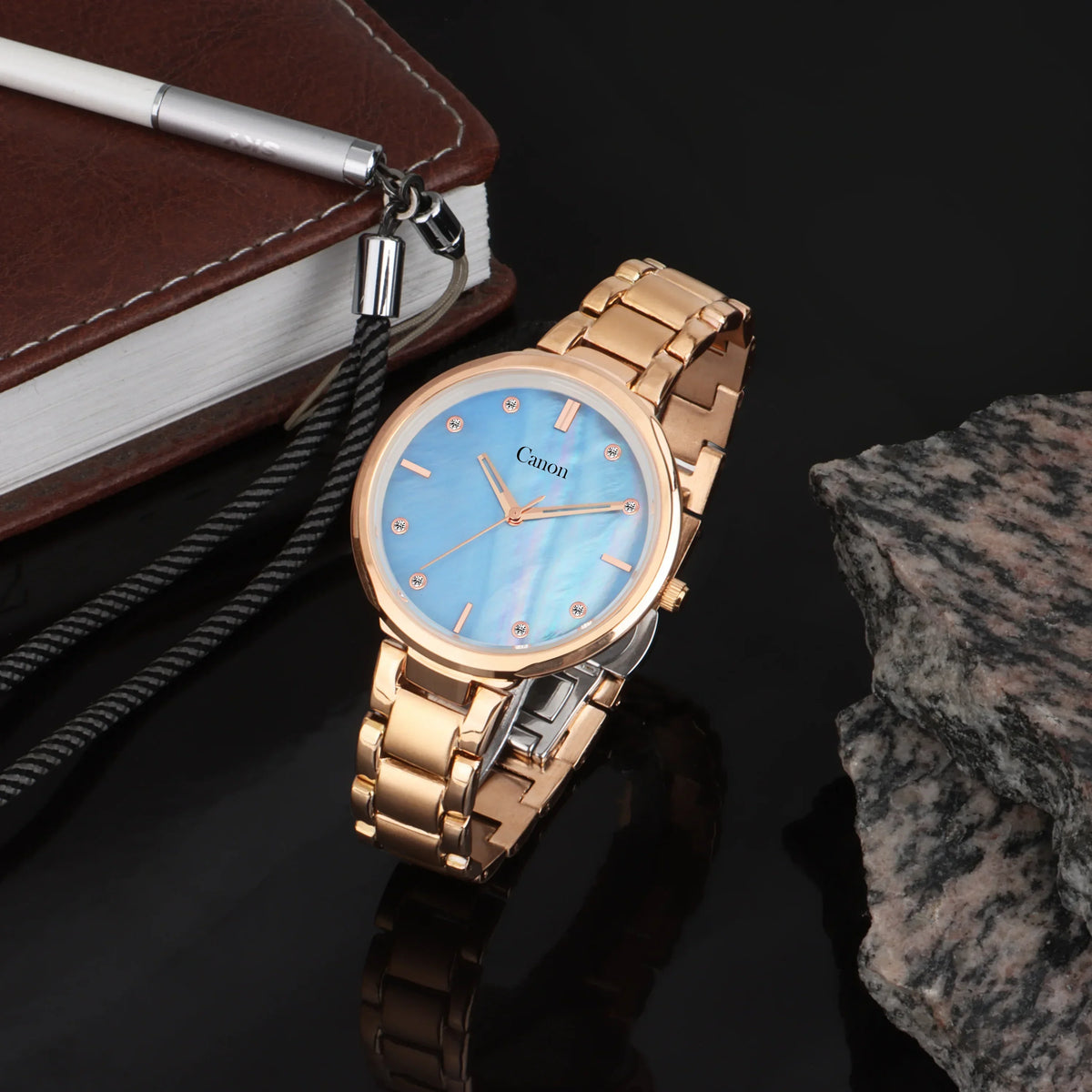 Gold analog wristwatch with blue dial and crystal markers on black stone background