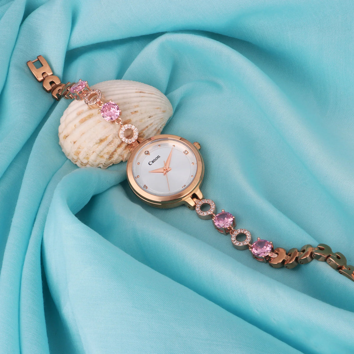 Elegant women's analog watch with pink crystal bracelet on aqua blue fabric background