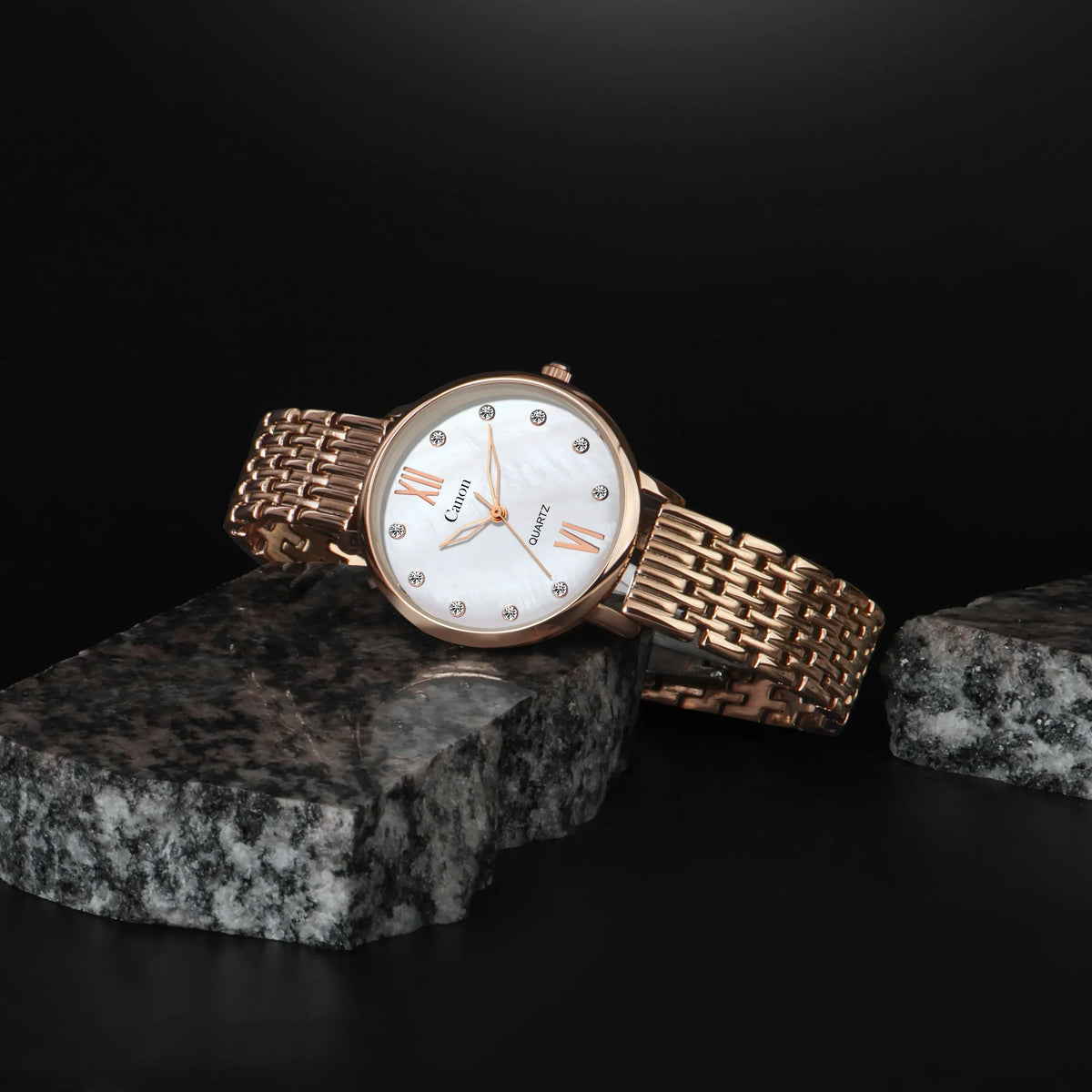 Elegant rose gold analog watch with white dial and crystal hour markers on dark stone background