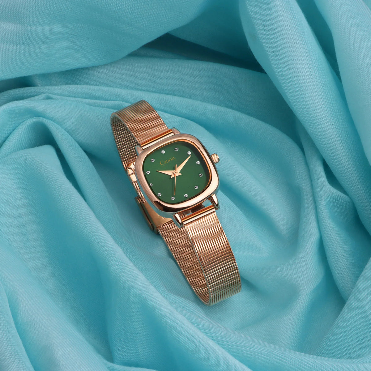 Gold mesh analog watch with green dial on blue fabric background