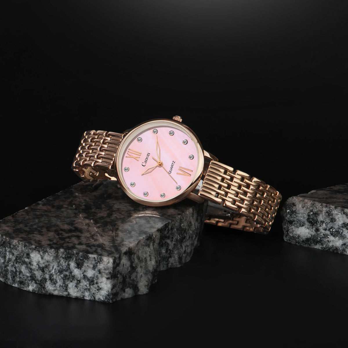 Rose gold analog watch with pink dial and metallic strap on a stone display, elegant style