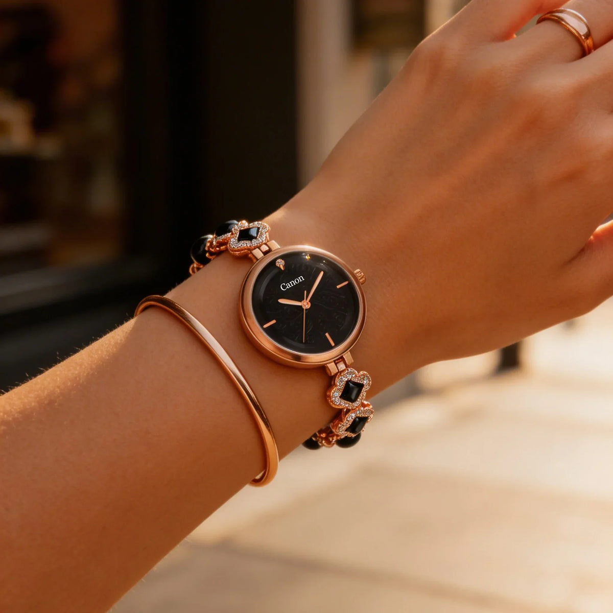 Elegant women's analog watch with black dial and rose gold bracelet on wrist outdoors