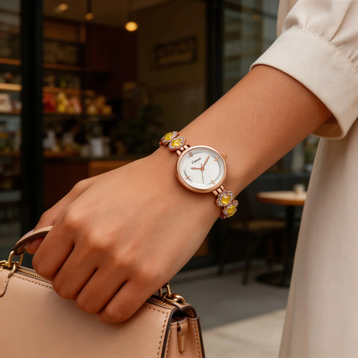 Elegant women's analog watch with floral band and gold accents, worn outdoors with a handbag