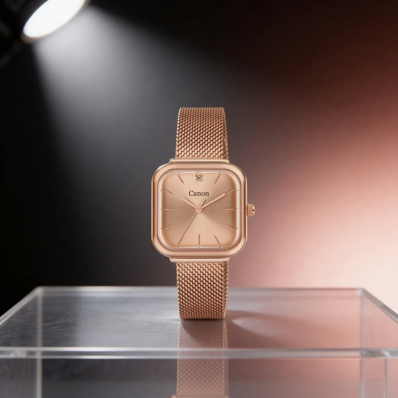 Rose gold Canon analog watch with mesh band, diamond accent, square case, displayed on glass stand under spotlight