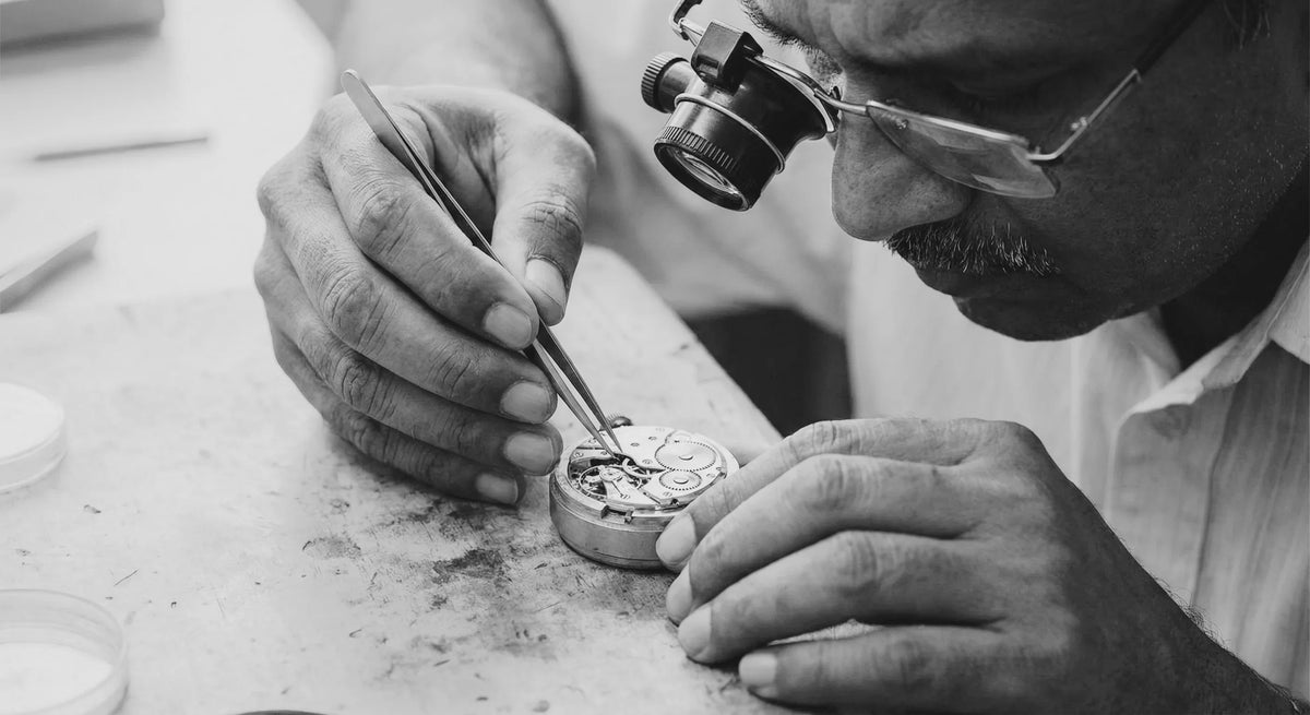 Watchmaker crafting precision analog quartz movement with tweezers and magnifier, showcasing expert craftsmanship.