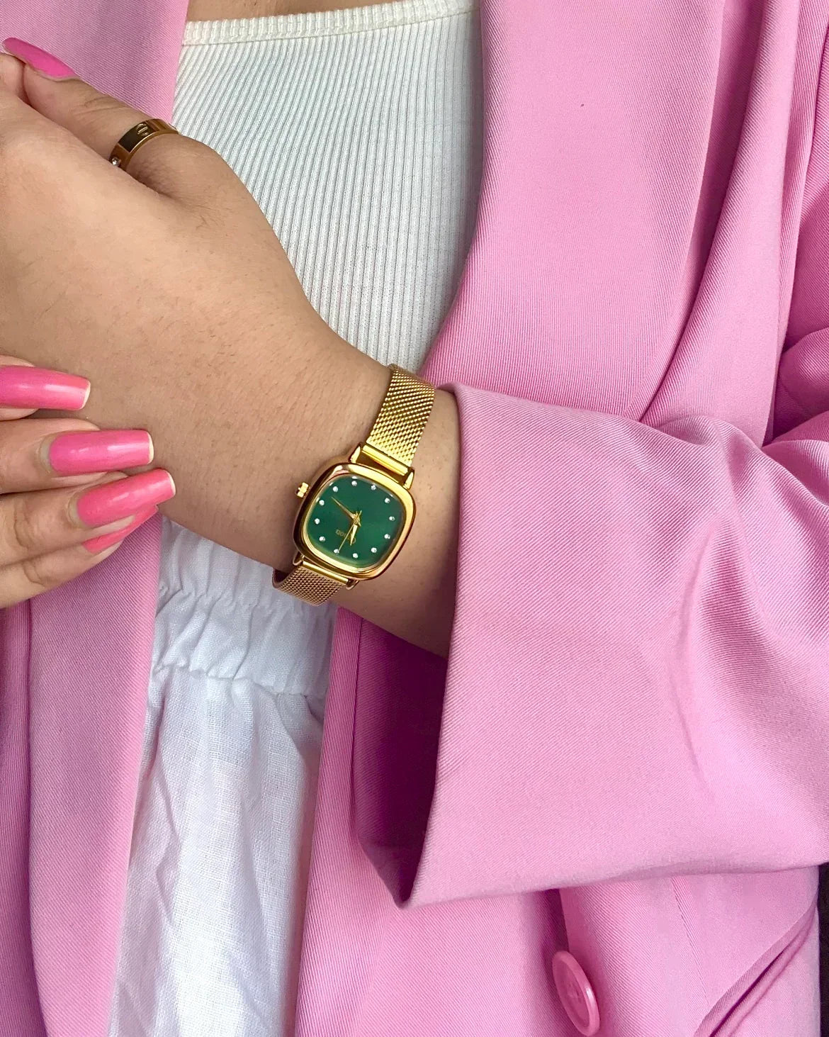 Gold mesh analog wristwatch with green dial worn with a pink blazer and white top