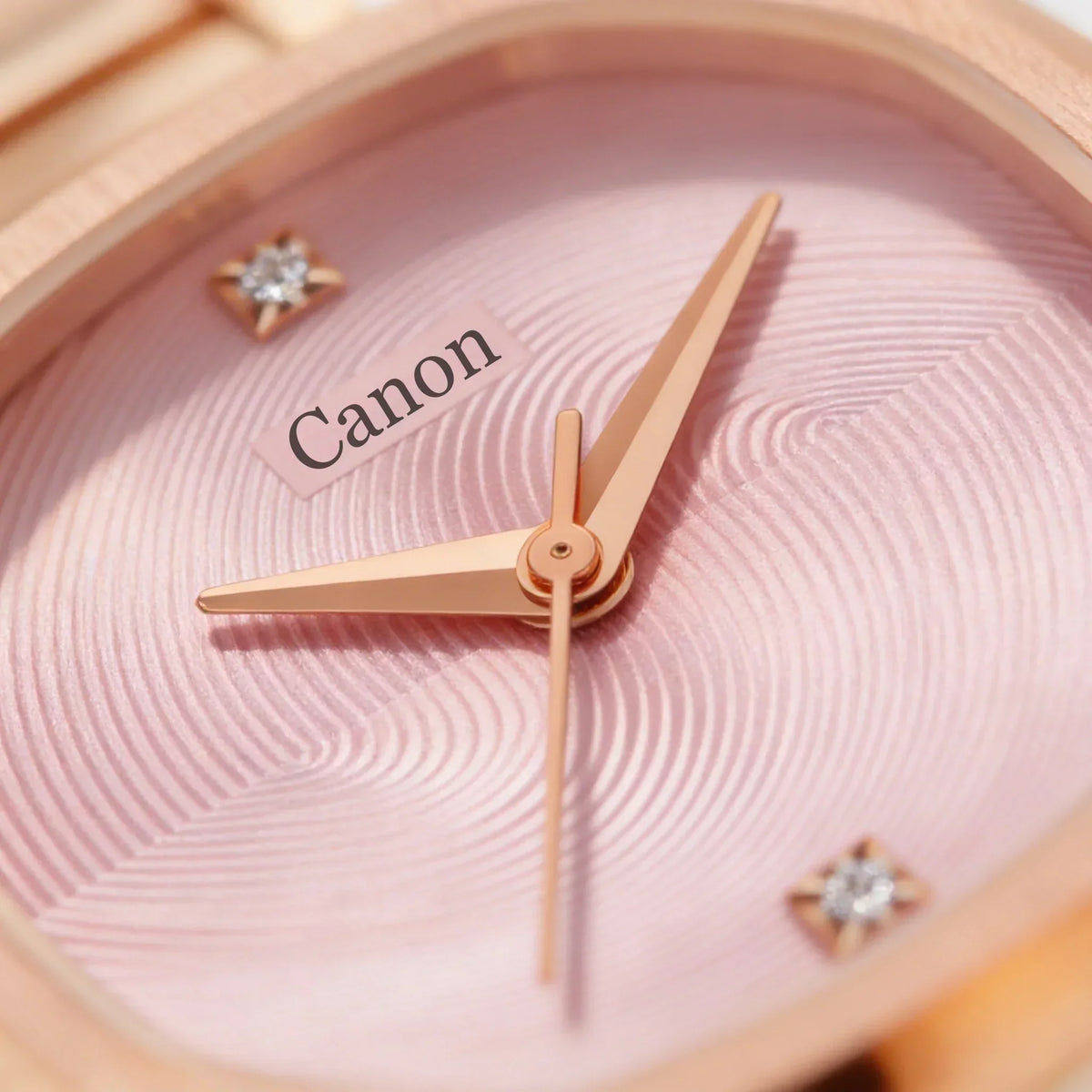 Close-up of an elegant analog watch with rose gold hands on a textured pink dial