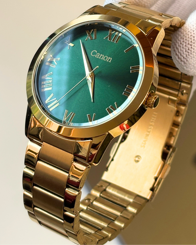 Gold wristwatch with a green face held by a gloved hand against a neutral background