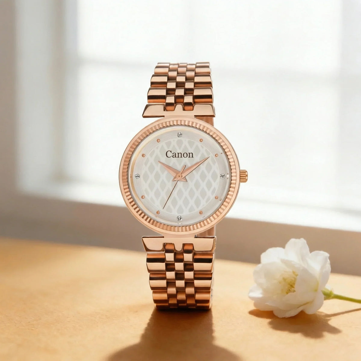 Elegant rose gold analog women's watch with patterned white dial on a table beside a flower