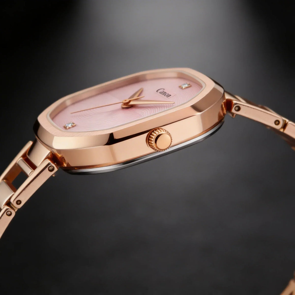 Rose gold analog wristwatch with pink face and linked bracelet on a dark background