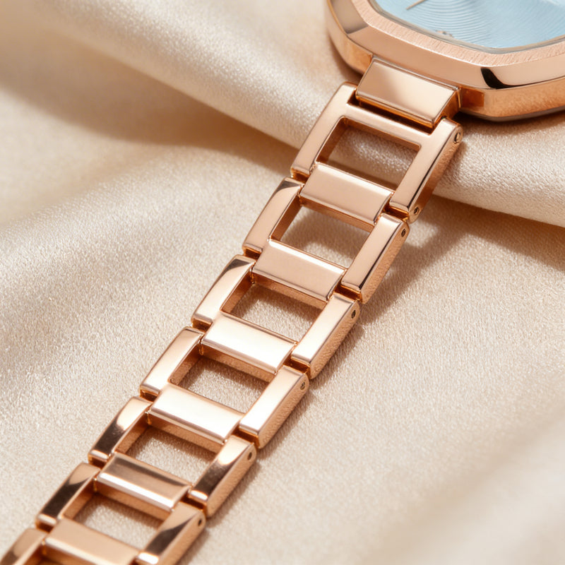 Close-up of a rose gold metal watch band on soft beige fabric, elegant analog style