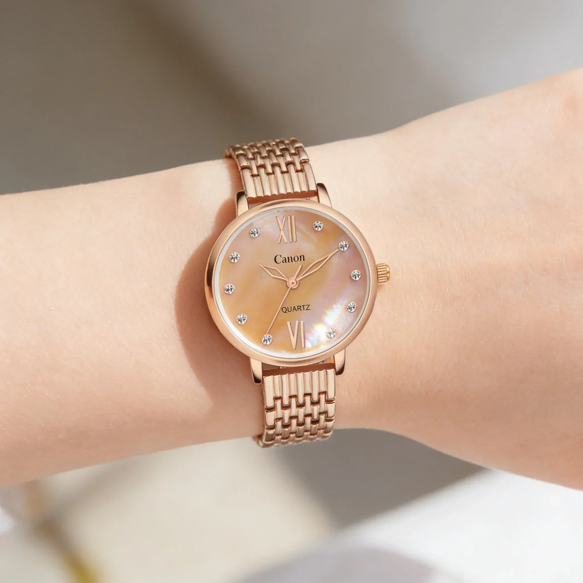 Rose gold analog women's watch with crystal markers and woven metal strap on wrist