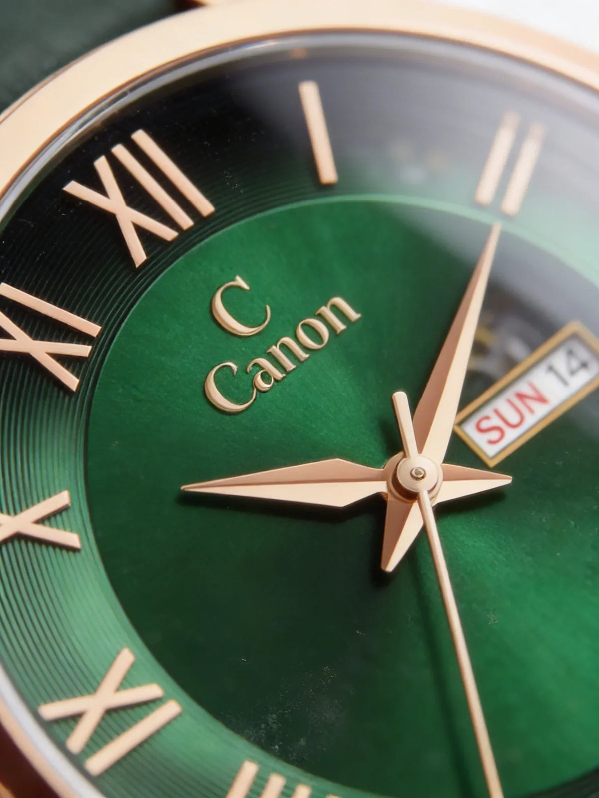 Close-up analog watch with green face, gold Roman numerals, day and date display