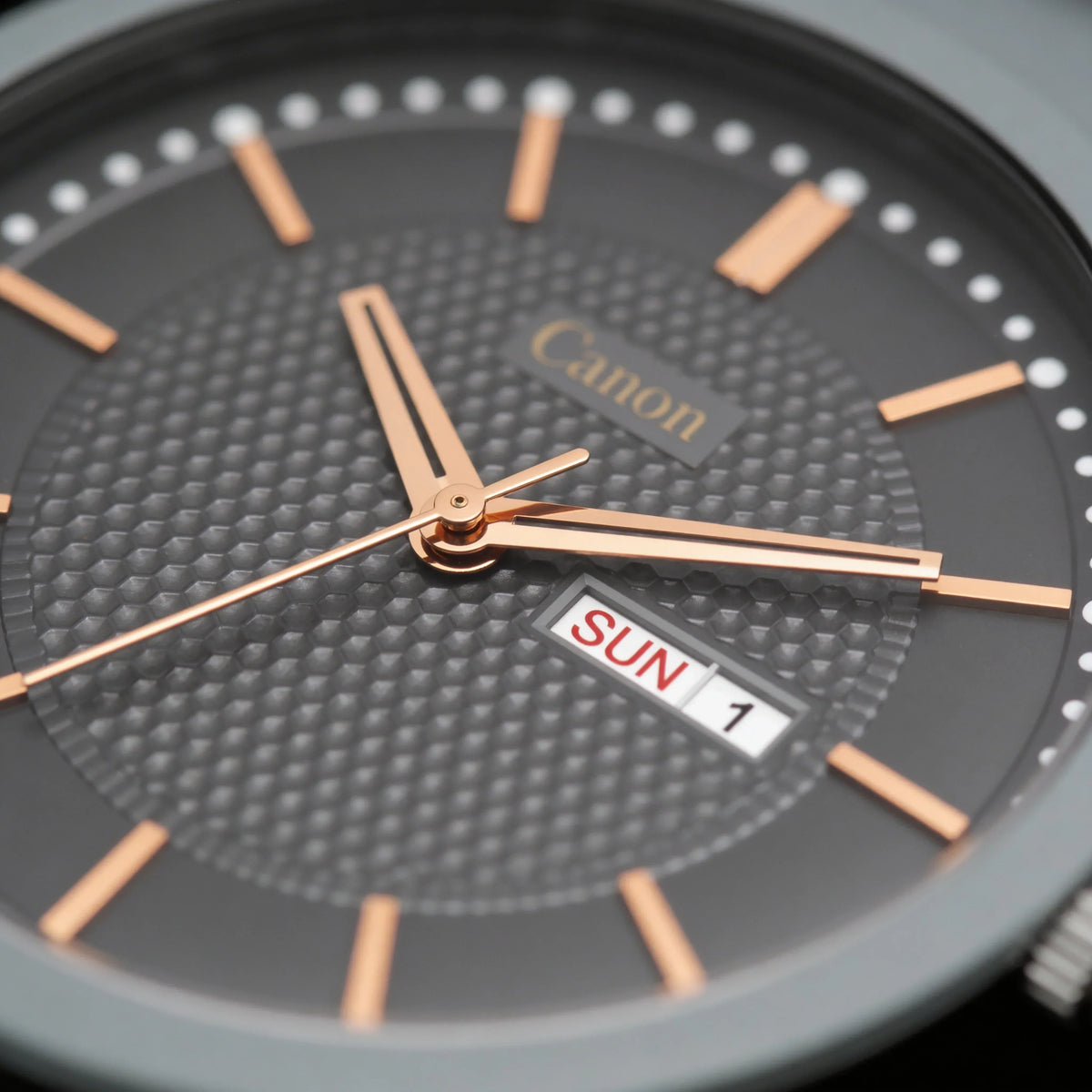 Close-up of a gray analog watch with rose gold hands, textured dial, and day-date display