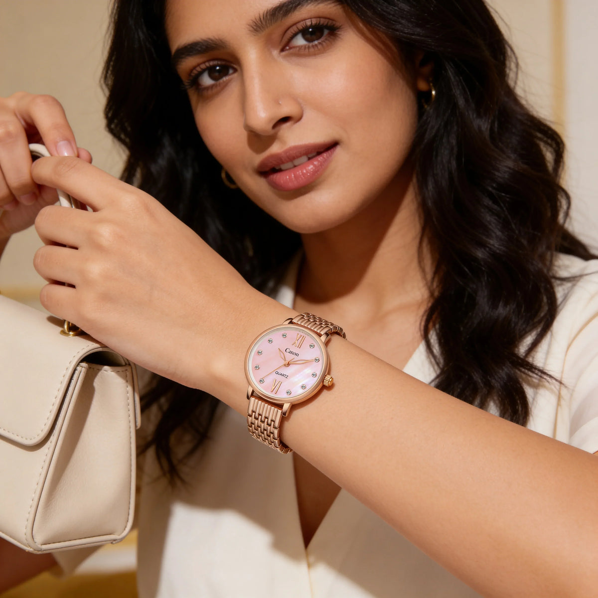 Woman wearing a rose gold analog watch with pink dial and crystal markers, holding a cream handbag