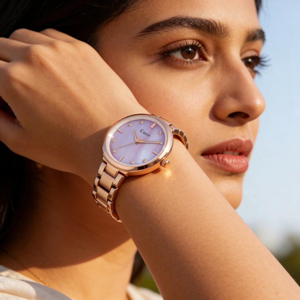 Woman wearing rose gold analog watch with pink dial and crystal markers outdoors