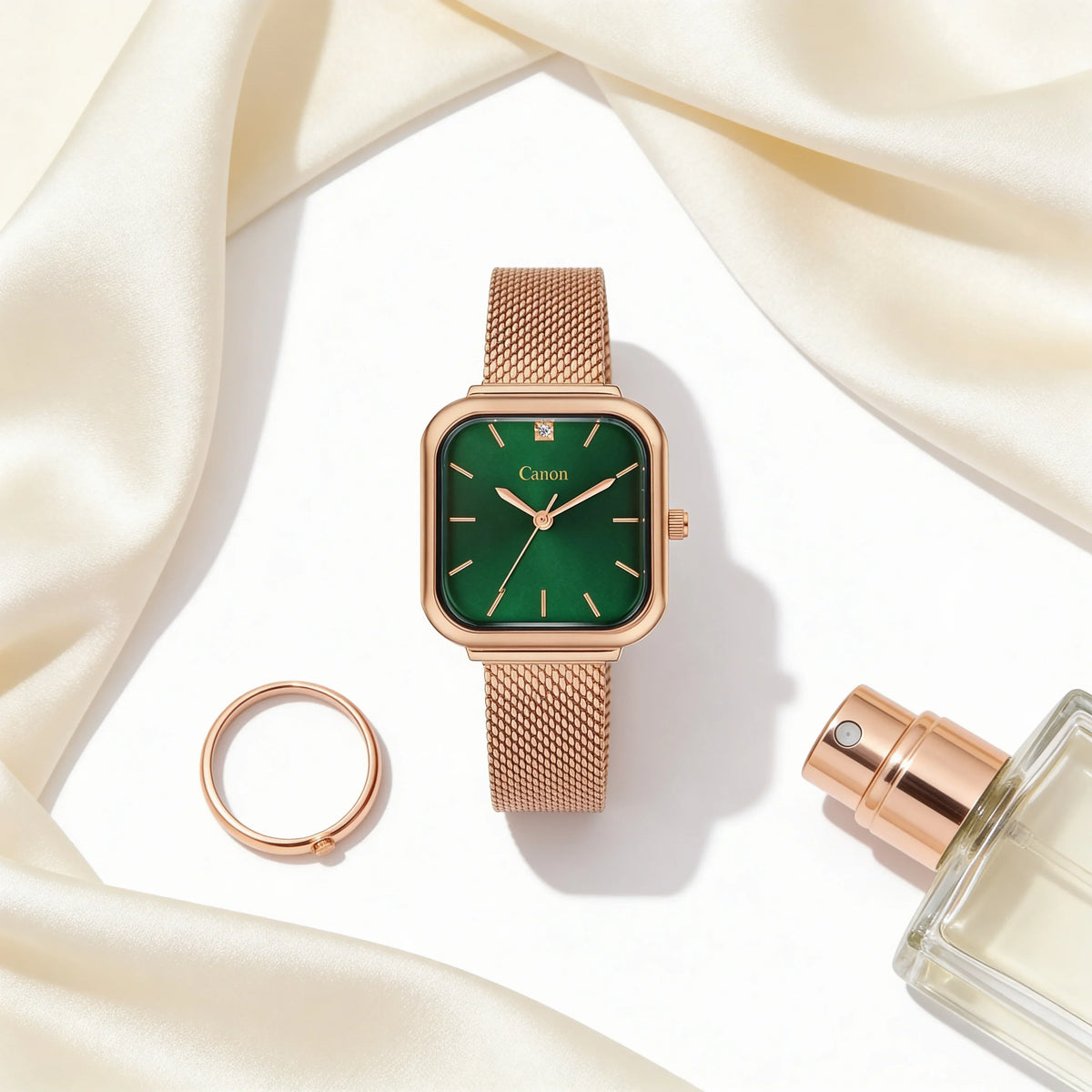 Rose gold mesh band analog watch with green dial, ring, and perfume on satin background