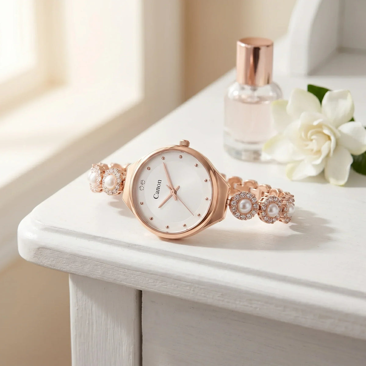 Elegant rose gold analog watch with pearl and crystal accents, displayed on white surface with flower and perfume bottle.
