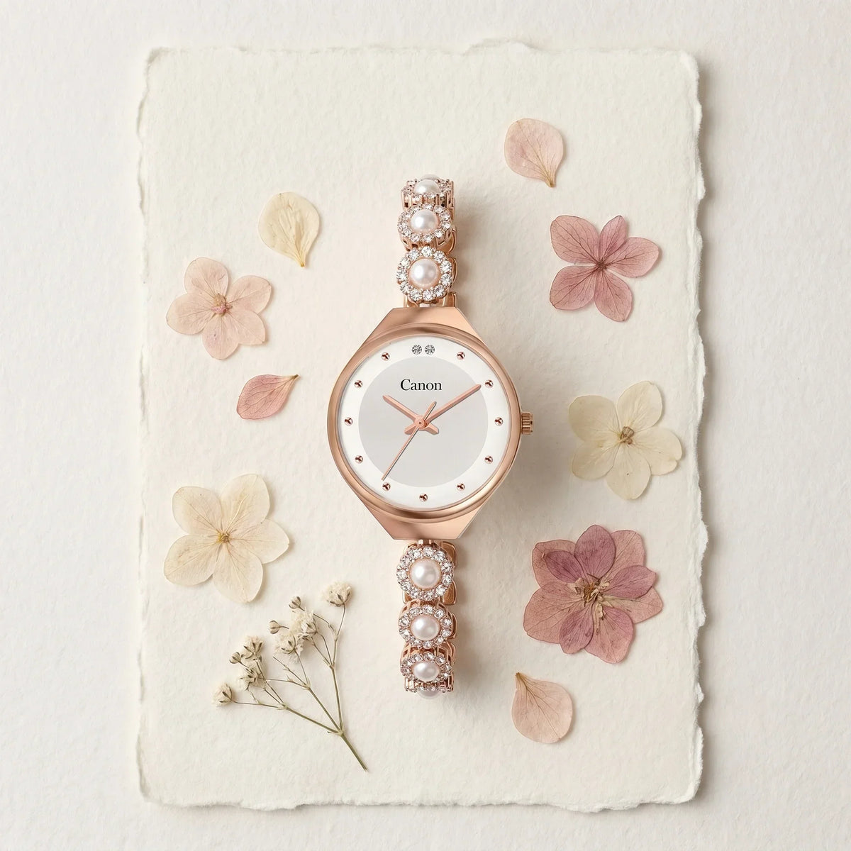 Elegant rose gold watch with pearl and crystal accents, displayed on textured paper with dried flowers.