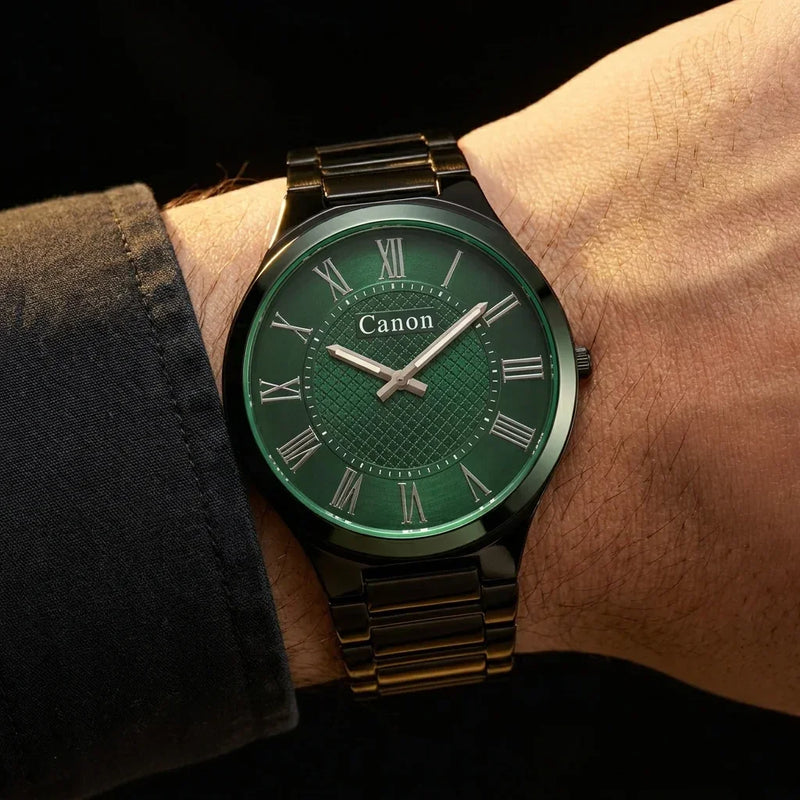 Green dial Canon watch with Roman numerals and black metal band on wrist