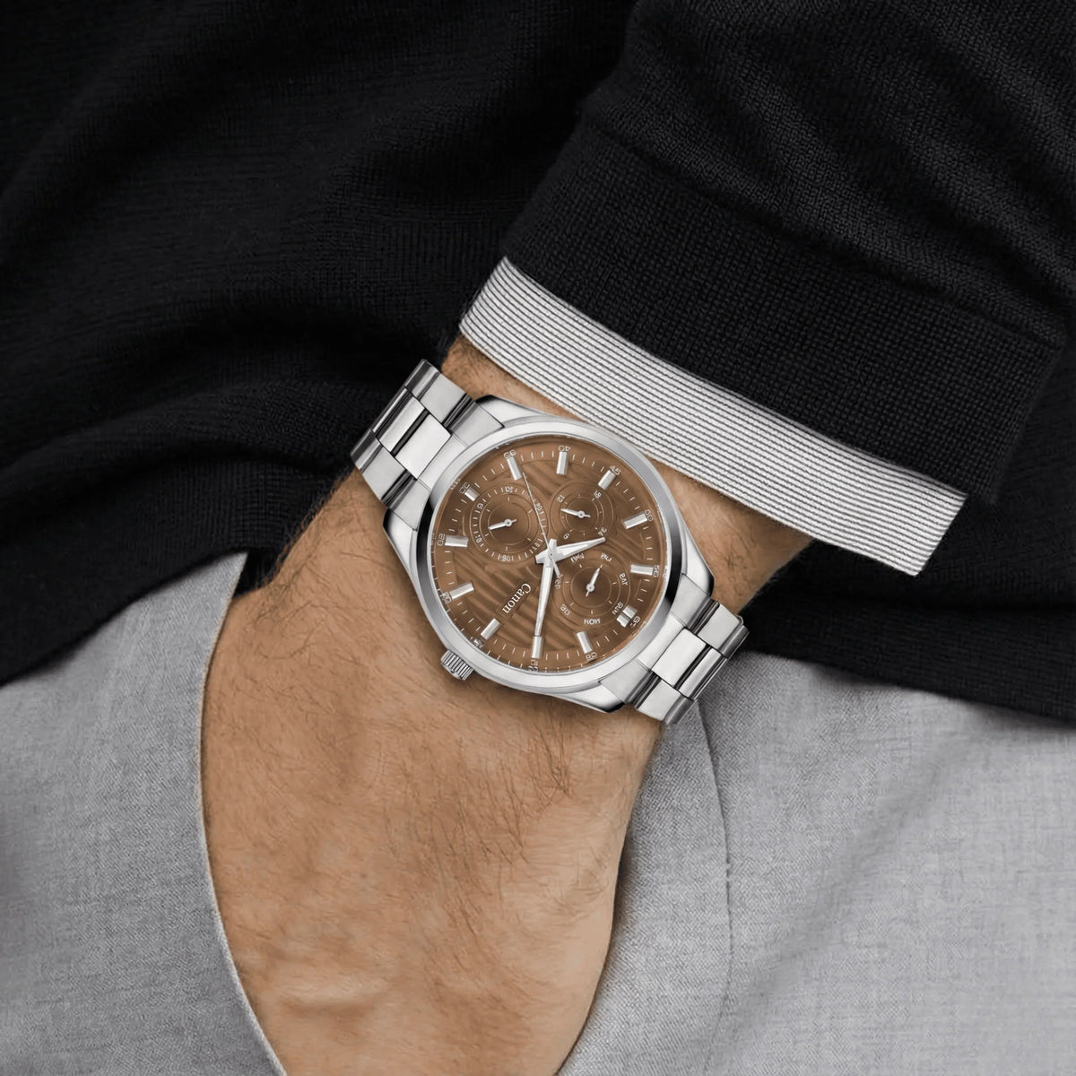 Men's silver analog watch with brown dial and multiple subdials on wrist, dressed in black sweater.